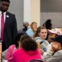 Albert Okwei stands by a table of students at a round table